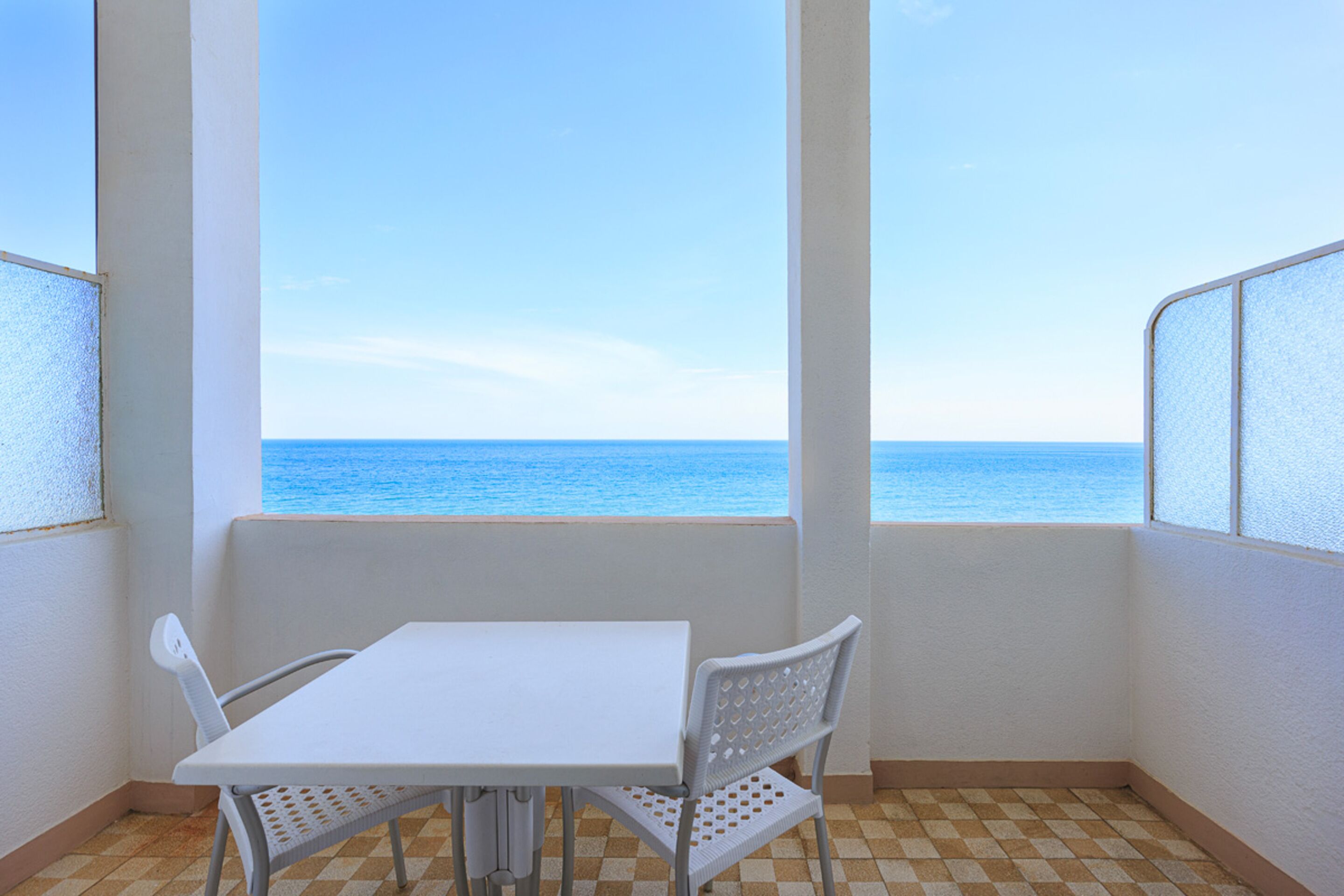 A balcony with a checkered floor, a white table, and two white chairs.
