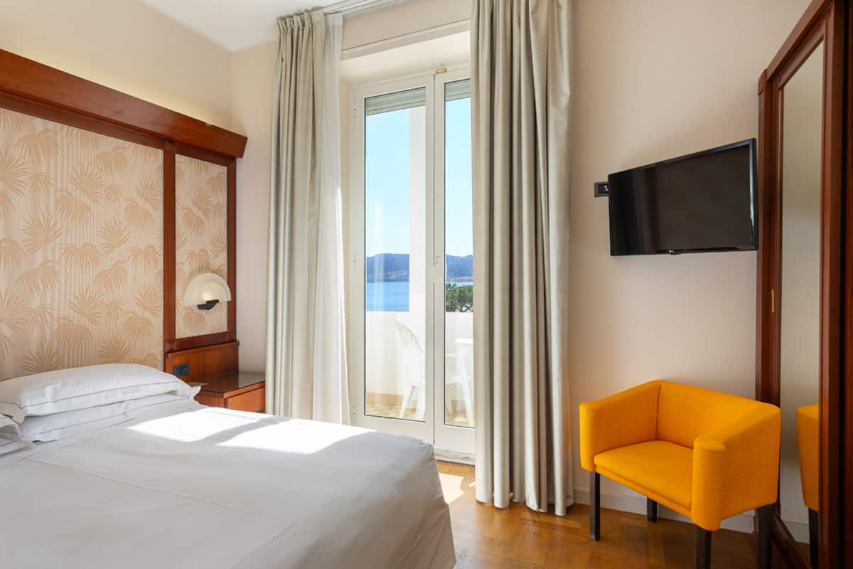 Ein Hotelzimmer mit Bett, Sessel, Fernseher und Blick ins Freie.