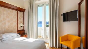 A hotel room with a bed, a chair, a TV, and a view of the outdoors.