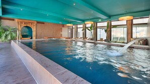 Una piscina interior con una cascada, rodeada de zonas de estar y grandes ventanales.