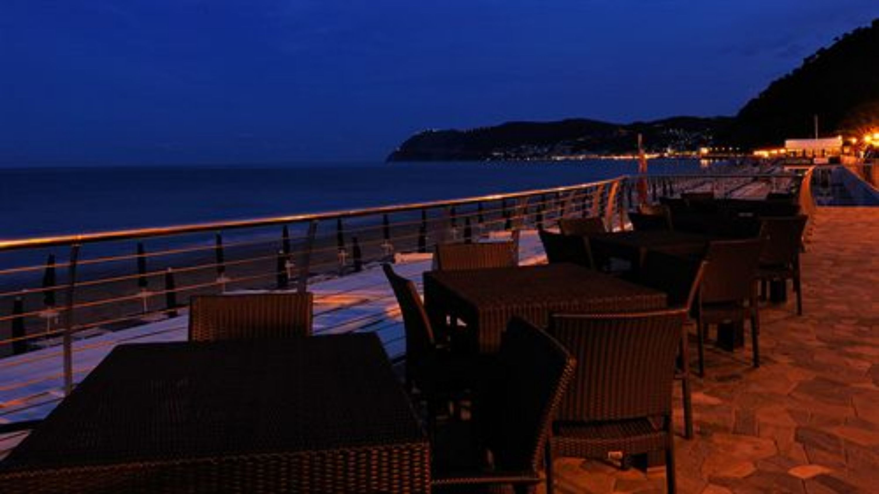 An outdoor seating area with wicker furniture and a view of the sea at dusk.