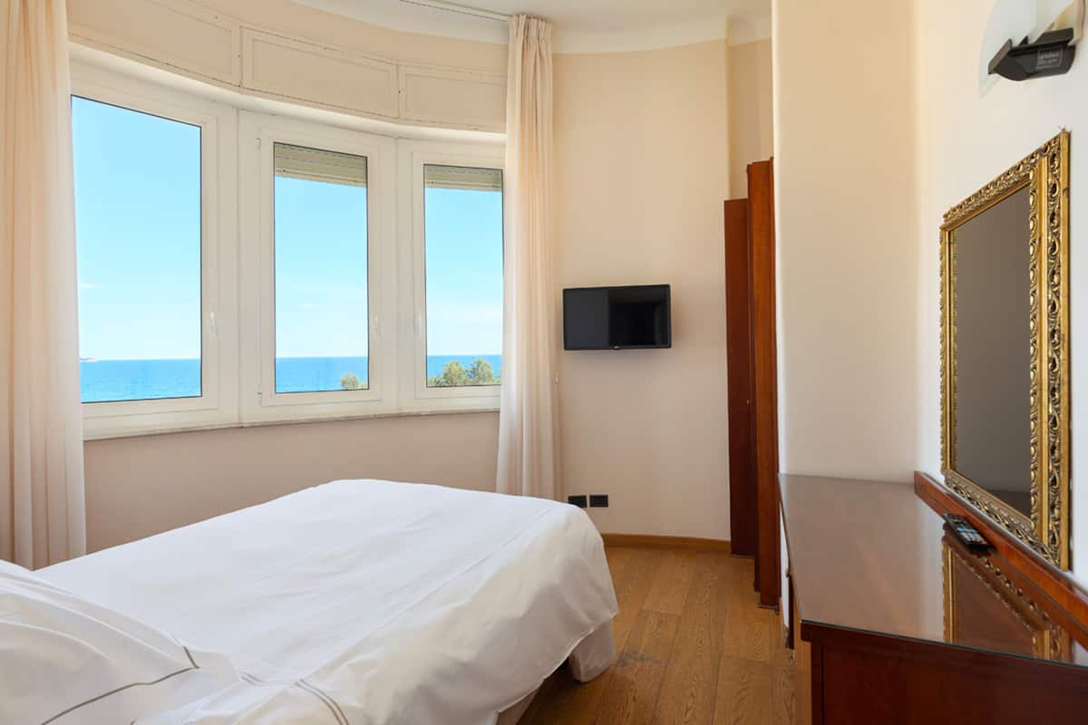 Ein Hotelzimmer mit Bett, Fernseher, Spiegel und Meerblick durch die Fenster.