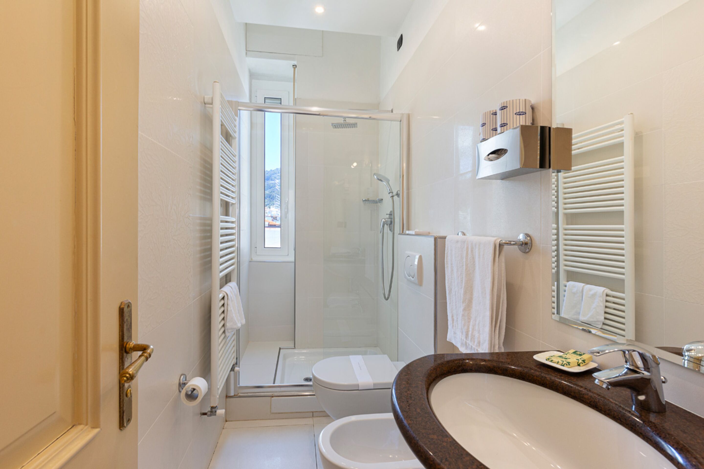 Un baño moderno con ducha envuelta en vidrio, inodoro blanco, lavamanos con encimera de mármol y toallero con toallas blancas.