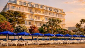 Un hotel frente a la playa con varios balcones, una fila de sombrillas azules y sillas reclinables blancas.