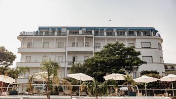 A multi-story hotel with balconies, outdoor seating with umbrellas, and a palm tree.
