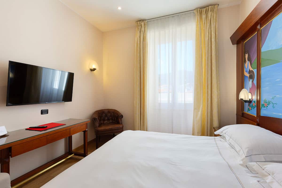 Ein Hotelzimmer mit Bett, Schreibtisch, Flachbildfernseher, Stuhl und einem fenster mit Vorhängen.