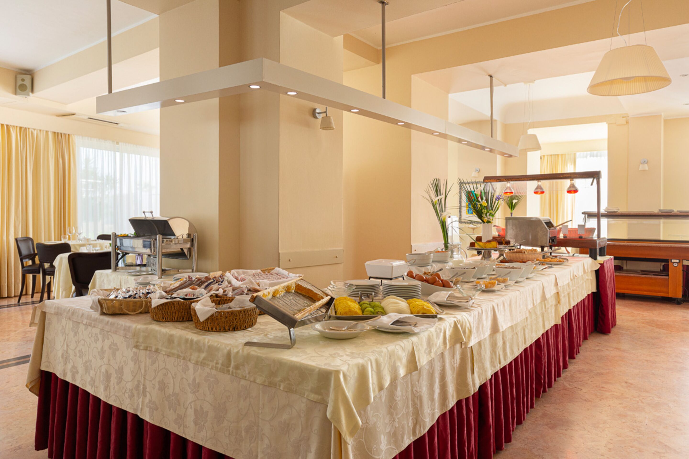A buffet setup with various food items and serving utensils on a table, surrounded by chairs and a dining area.
