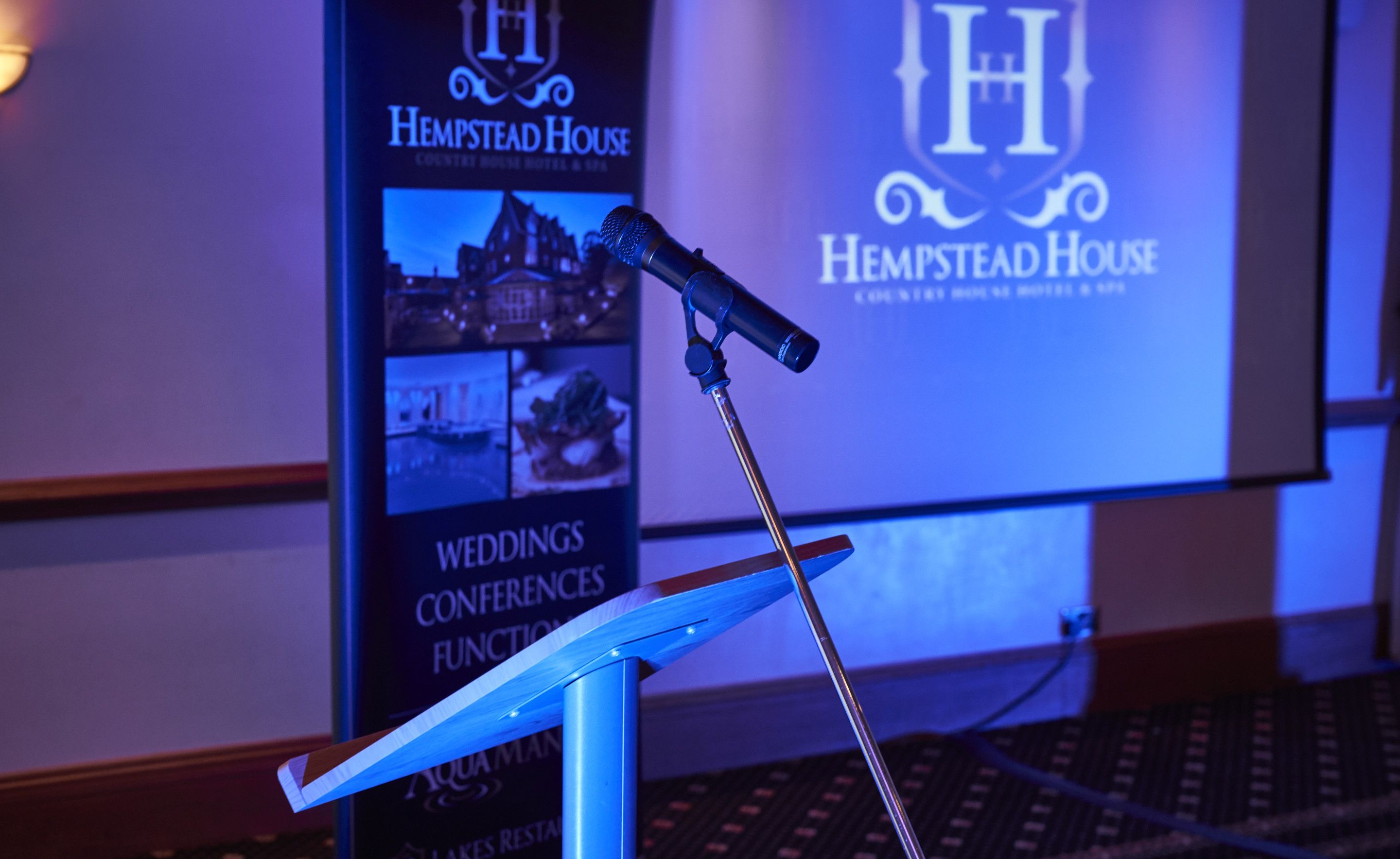 A microphone on a stand in front of a backdrop with the Hempstead House logo and text indicating it is a conference room.
