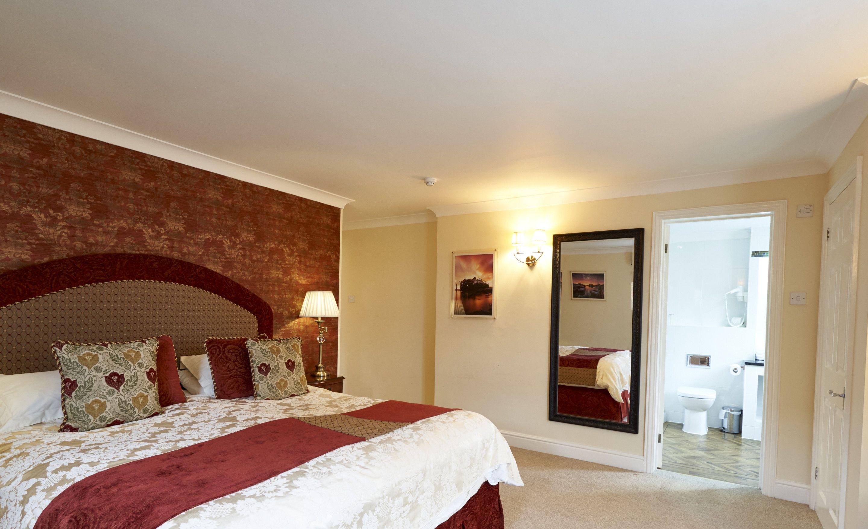Une chambre d’hôtel avec un grand lit, un miroir, une table de chevet avec une lampe et une porte donnant sur une salle de bain.