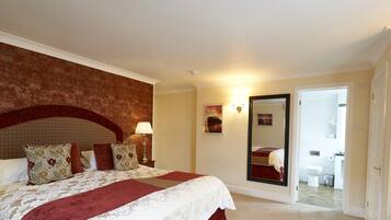 Une chambre d’hôtel avec un grand lit, un miroir, une table de chevet avec une lampe et une porte donnant sur une salle de bain.