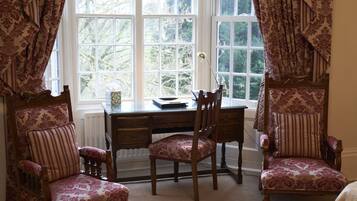 A room with a wooden desk, two chairs, a radiator, and a window with curtains.