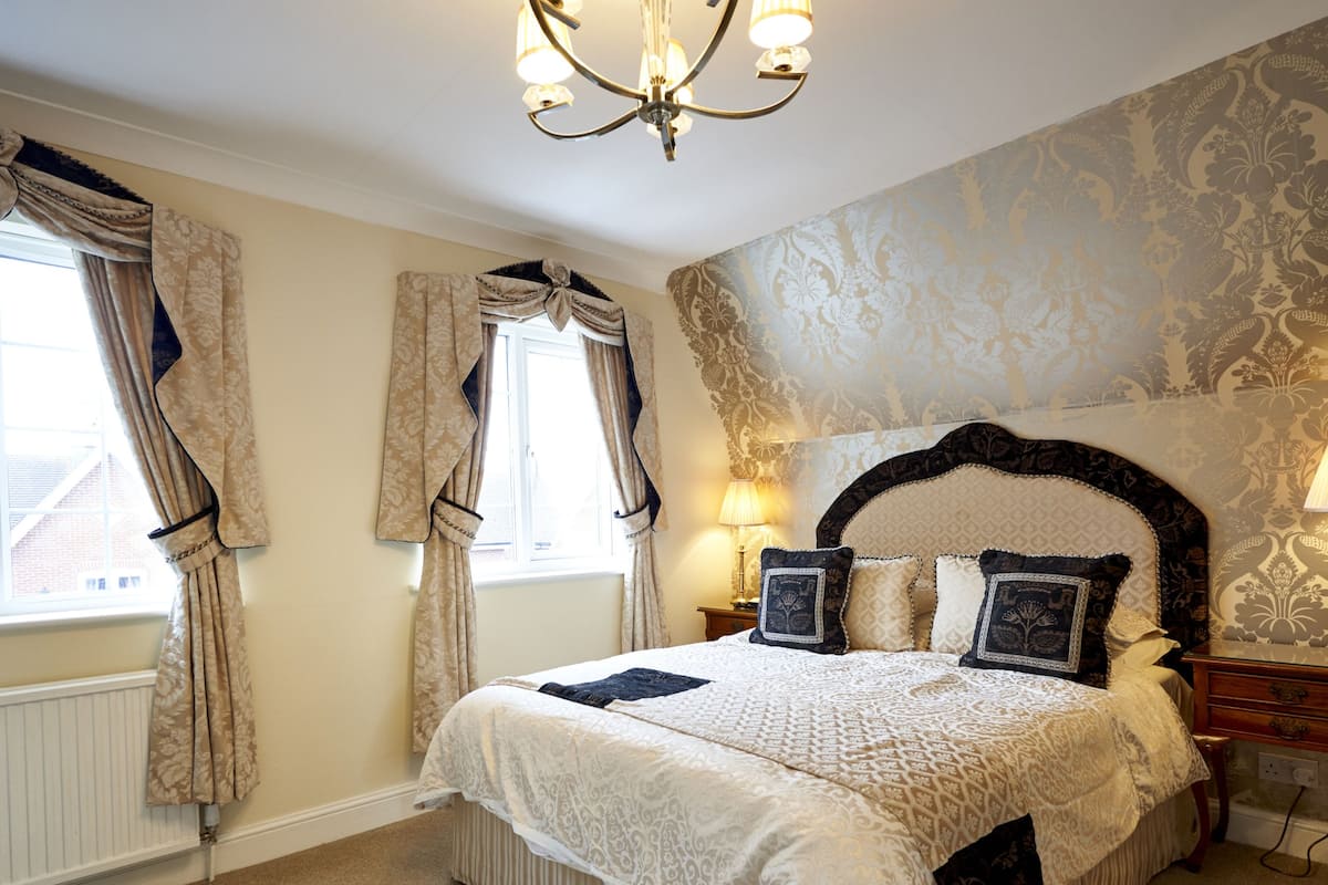A bedroom with a large bed, a chandelier, and patterned wallpaper.