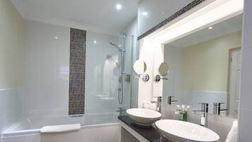 Un baño moderno con ducha de mampara de vidrio, dos lavamanos y un espejo grande.