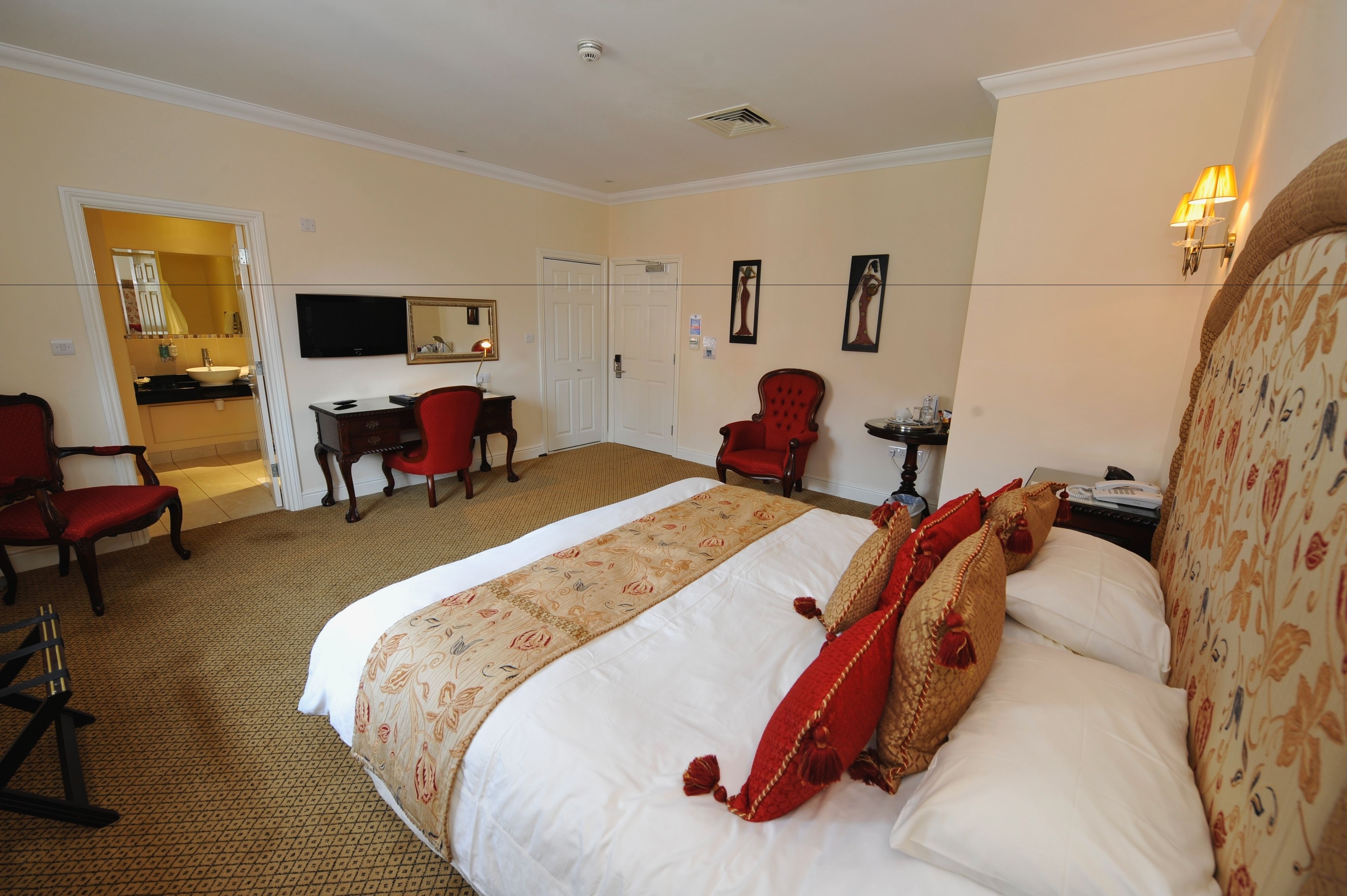 A hotel room with a large bed, two red chairs, a desk, a television, and a mirror.