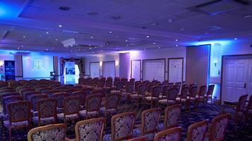 A conference room with rows of patterned chairs, a stage with a presentation screen, and a banner.