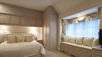 A bedroom with a large bed, built-in wardrobe, bedside seating, and a window with curtains.