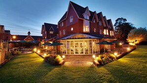 A large, multi-story building with a prominent glass facade, a well-maintained lawn, and outdoor seating areas with umbrellas. - Hempstead House Hotel (Sittingbourne)
