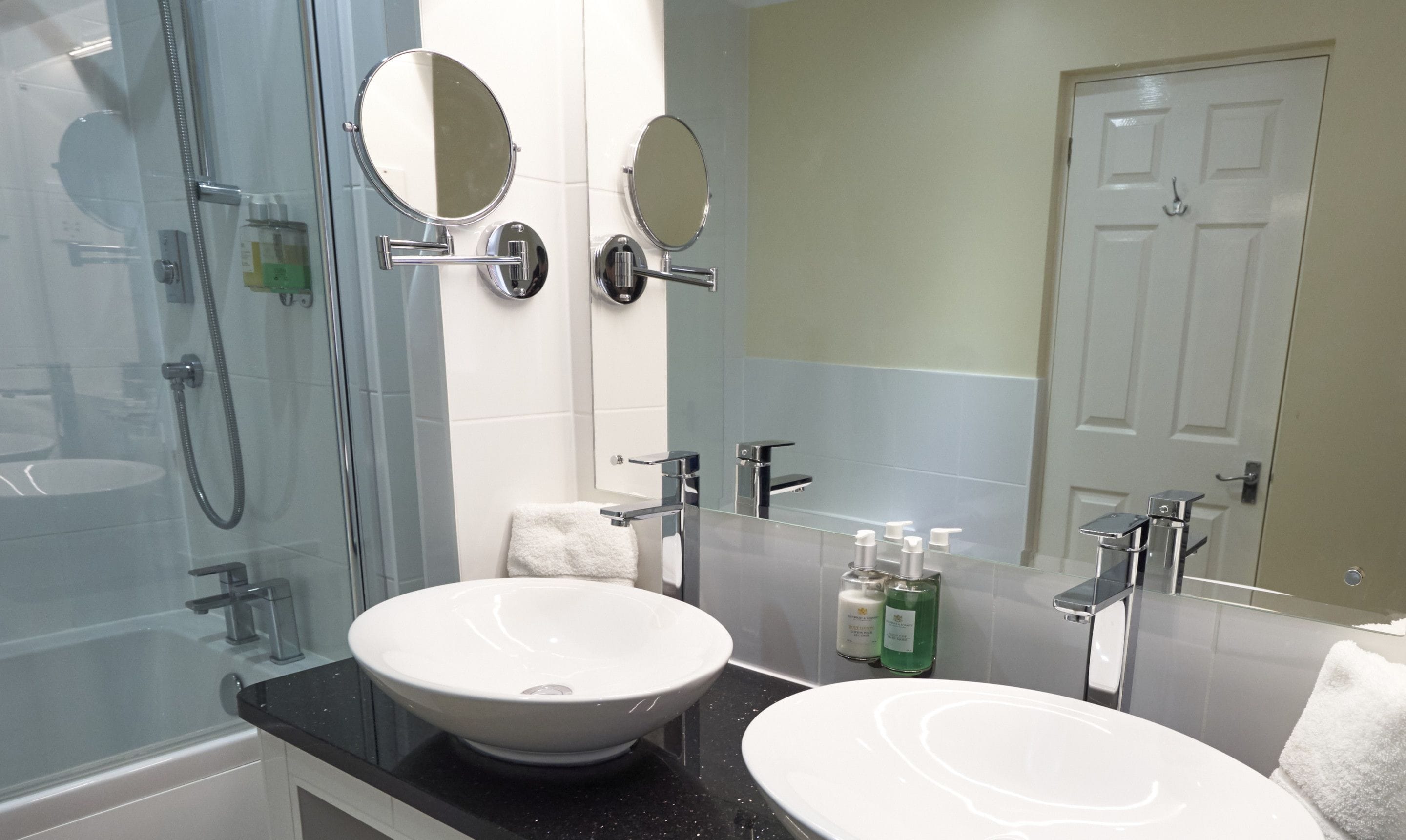A modern bathroom with a glass shower enclosure, two sinks, and a large mirror.