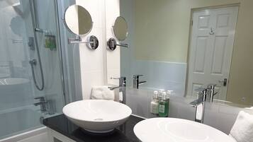 A modern bathroom with a glass shower enclosure, two sinks, and a large mirror.