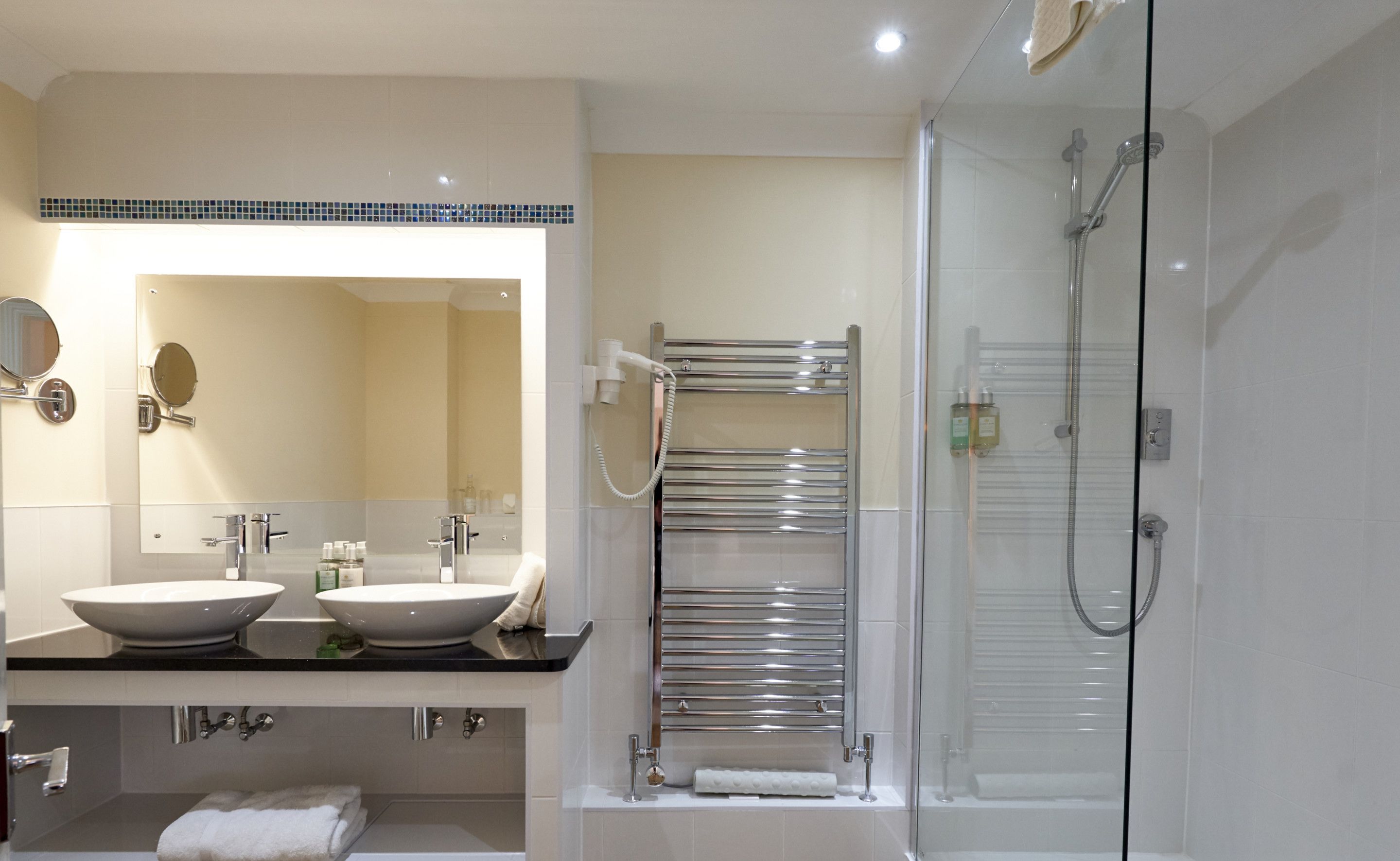 A modern bathroom with two sinks, a glass shower enclosure, and a towel rack.