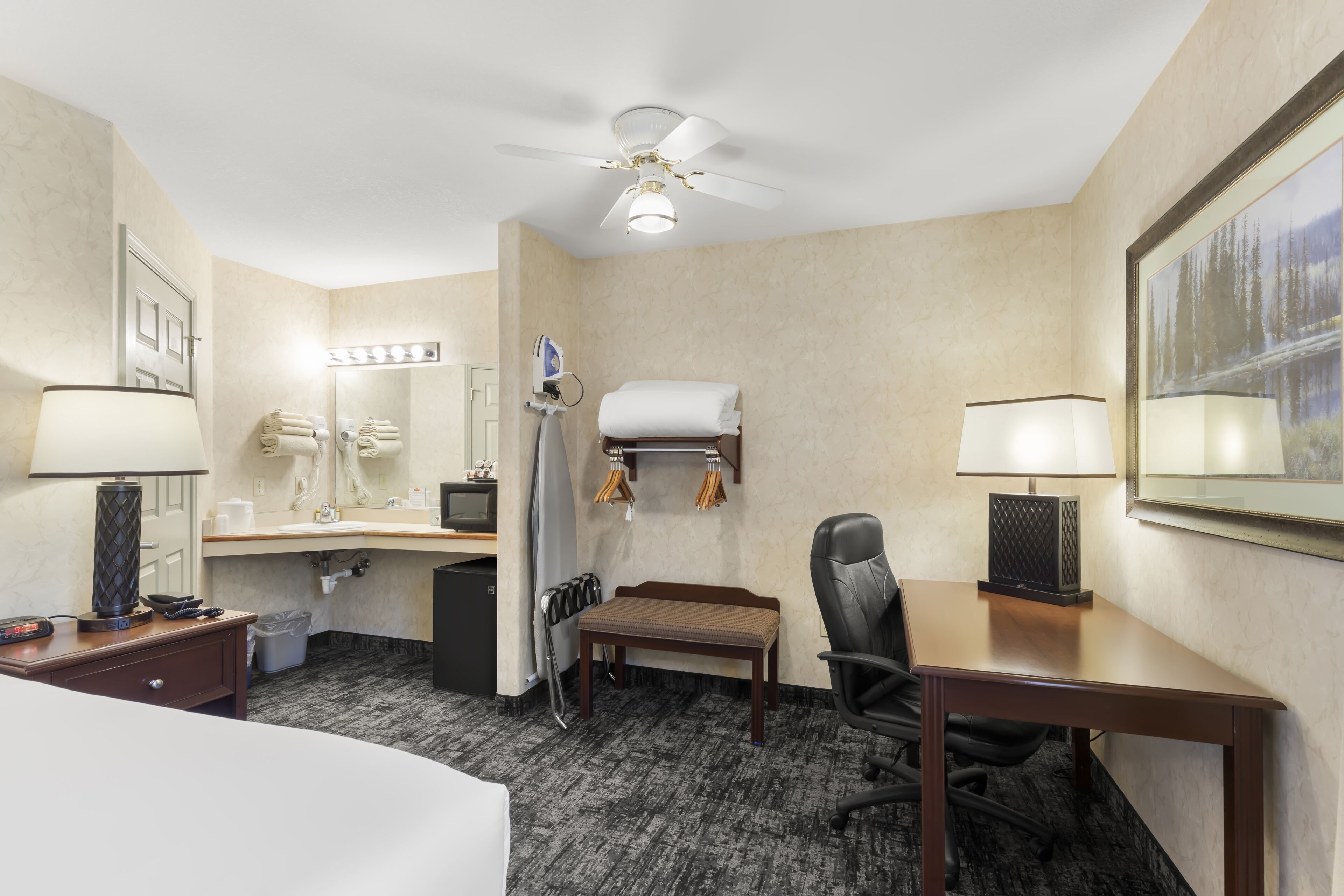 Habitación de hotel con cama, escritorio, silla y ventilador de techo.