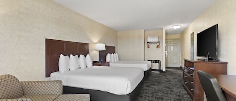 A hotel room with two beds, a desk, a TV, and a patterned sofa.