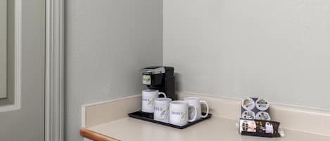 A coffee station with a coffee machine, three white mugs, and a tray with coffee pods.