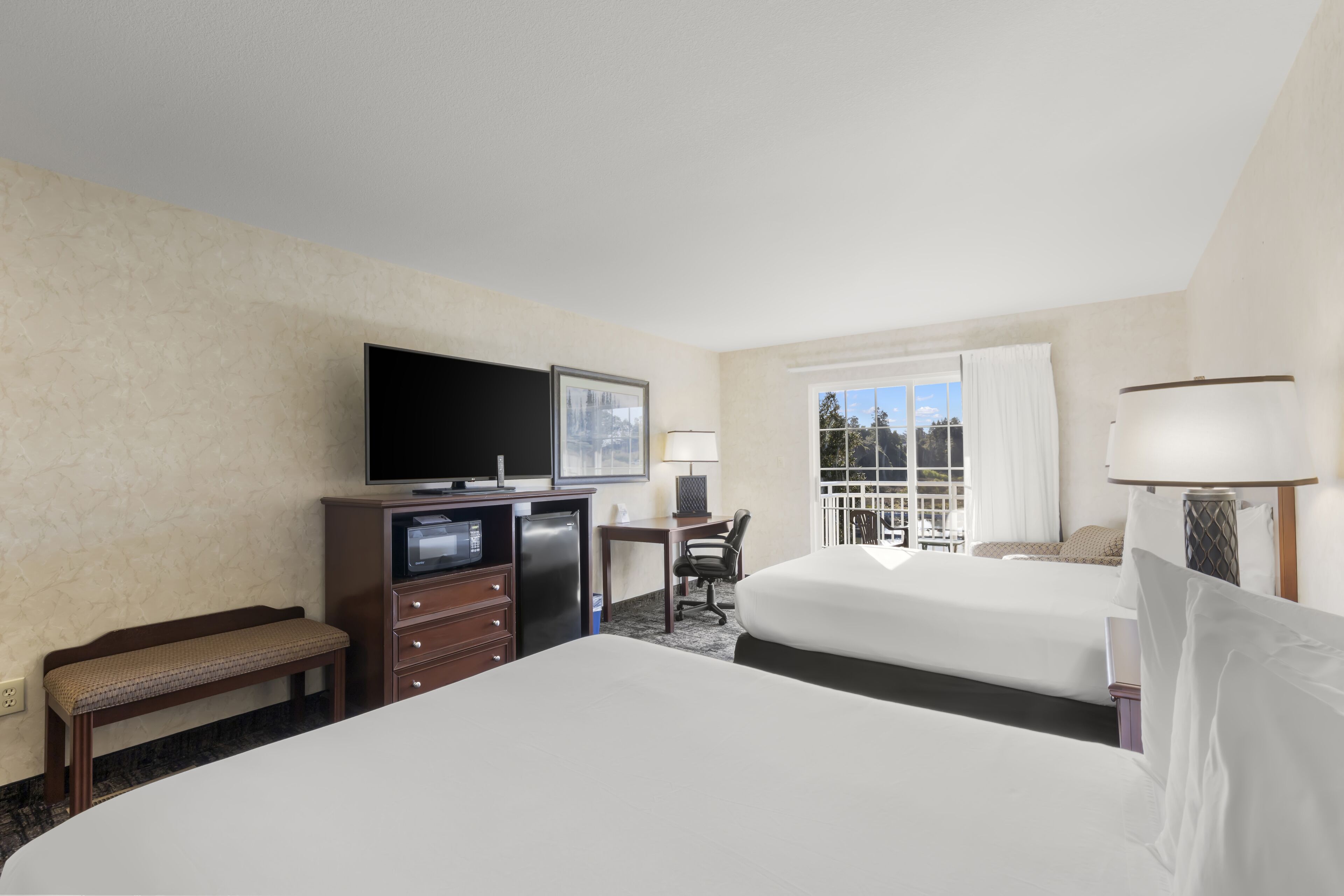 A hotel room with two beds, a desk, a television, and a window with curtains.