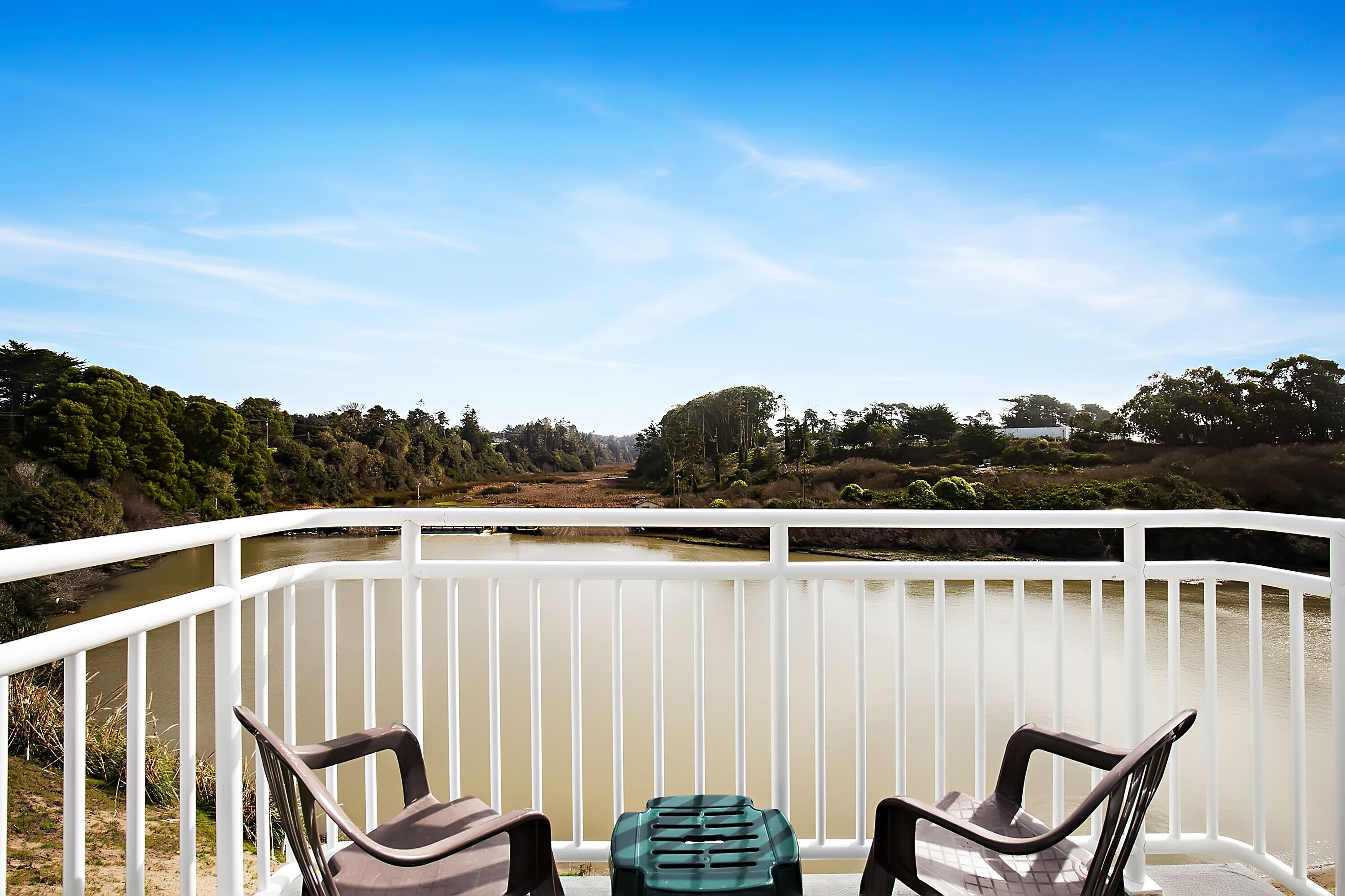 A balcony with two chairs and a small table, overlooking a river and greenery.