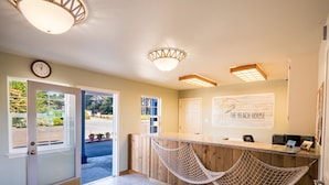 A reception area with a wooden counter, a hammock, a clock, and a sign for The Beach House in California. - The Beach House Inn (Fort Bragg)