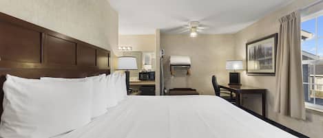Una habitación de hotel con una cama grande, un escritorio con silla, un microondas y un ventilador de techo.