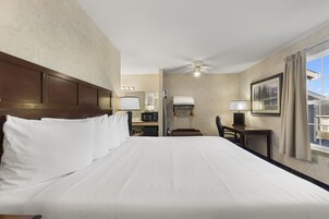 A hotel room with a large bed, a desk with a chair, a microwave, and a ceiling fan.