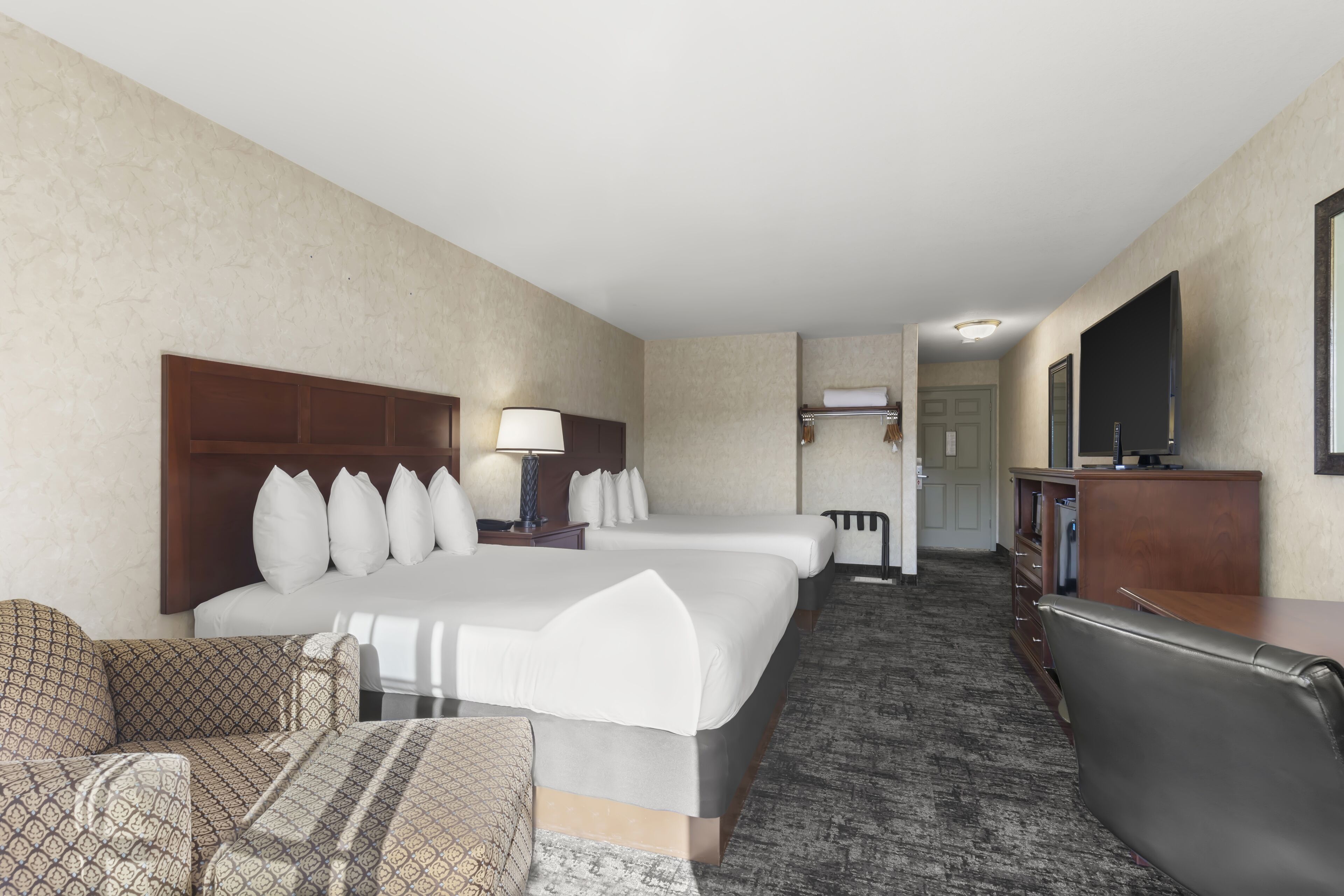 A hotel room with a large bed, two bedside tables, a desk, a chair, and a television.