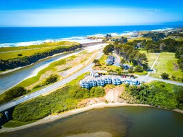 An aerial view of a coastal area with a bridge, a beach, and a row of blue buildings with a parking lot.