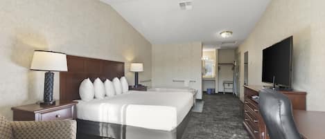 A hotel room with a large bed, a desk with a chair, a television, and a bathroom visible in the background.