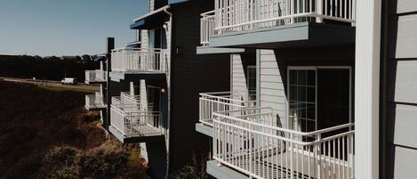 A modern building with multiple balconies, each with white railings and glass doors.