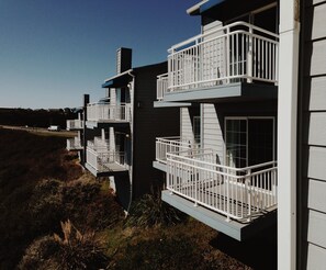 A modern building with multiple balconies, each with white railings and glass doors.