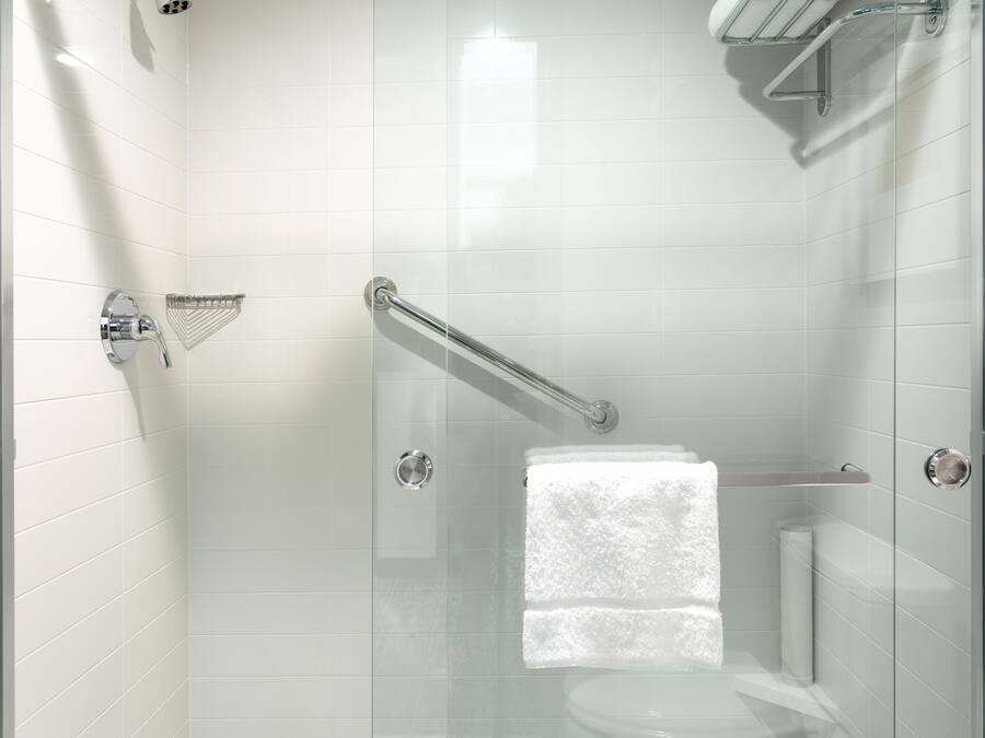 Una ducha moderna con puerta de cristal, cabezal de ducha manual y un perchero para toallas.