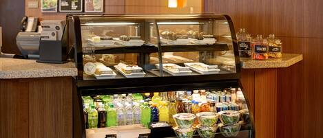 A coffee shop counter with a display case of pastries and a refrigerated section with various beverages.
