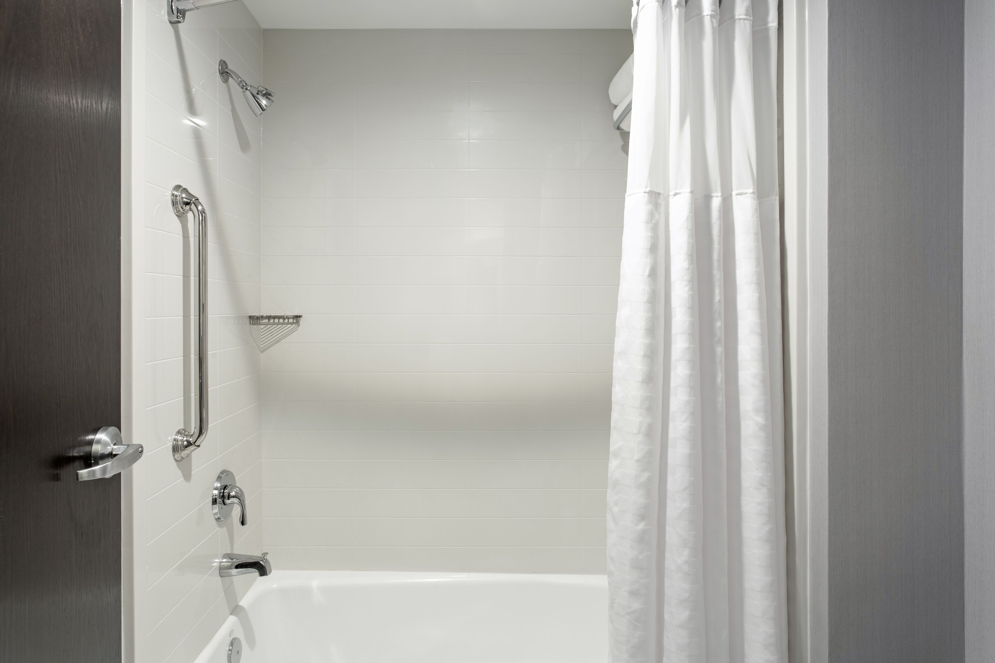 A bathroom with a white bathtub, a shower with a handheld showerhead, and a grab bar.