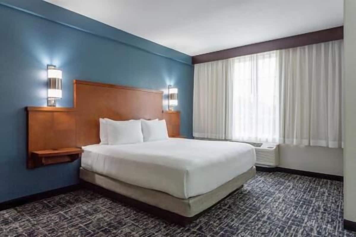 A hotel room with a large bed, a wooden headboard, two bedside tables, and a window with curtains.
