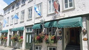 A white building with green awnings, multiple flags, and flower baskets. - Hotel Acadia (Québec City)