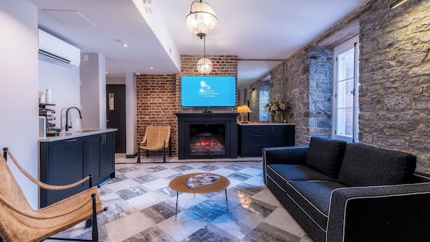 A modern living room with a fireplace, a sofa, a coffee table, and a TV. - Hotel Acadia (Québec City)