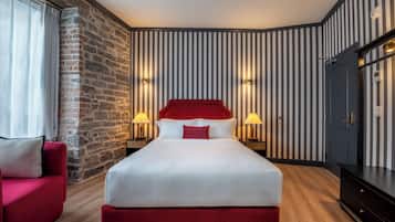 Ein Hotelzimmer mit einem großen Bett, einem roten Sitzsofa, einer Wand aus Stein und gestreifter Tapete.
