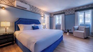 A modern hotel room with a large bed, bedside lamps, a small table, a sofa, and a window with curtains.