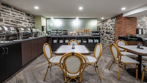 A restaurant with a brick wall, a buffet with various food items, and a seating area with tables and chairs. - Hotel Acadia (Québec City)