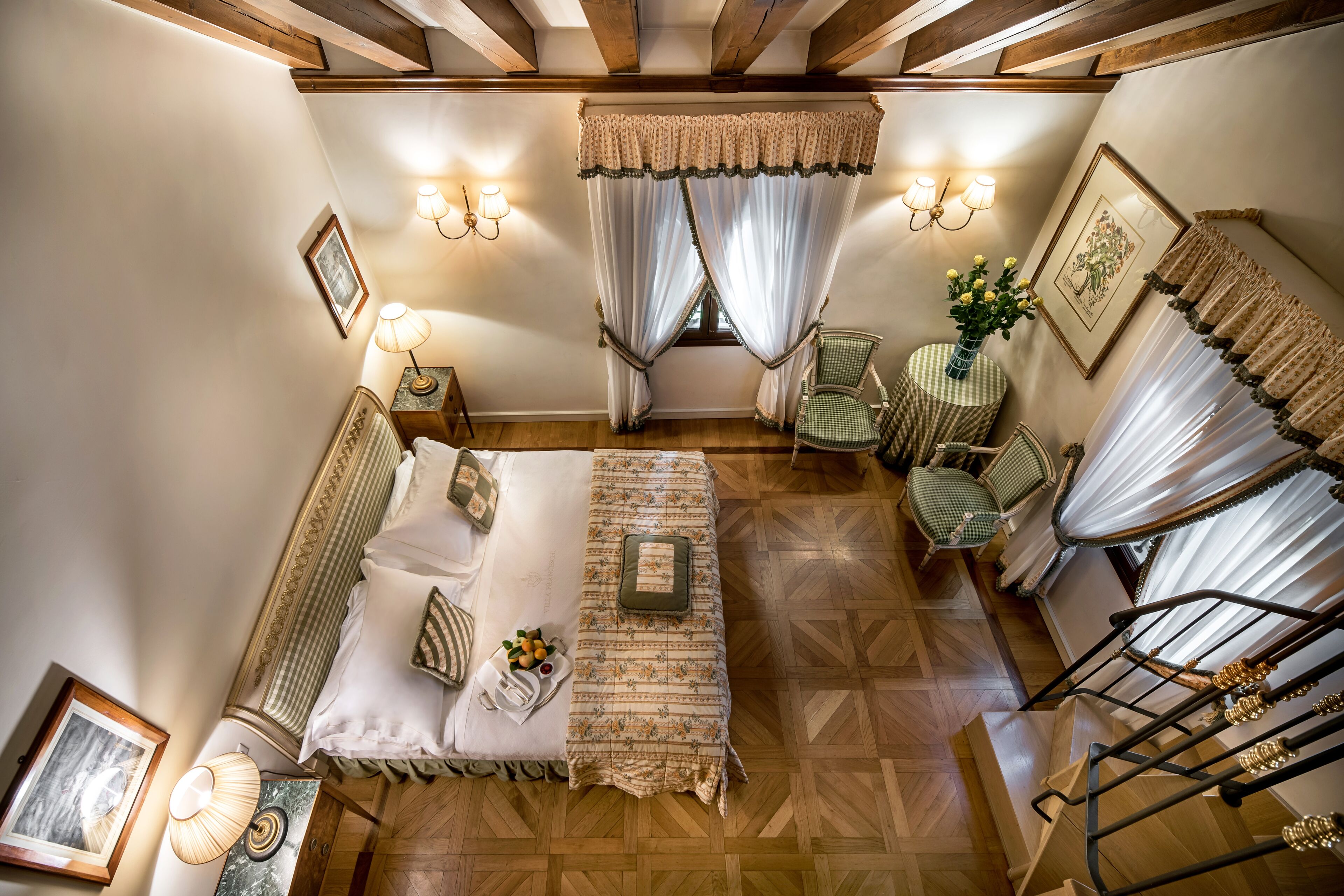 A bedroom with a bed, bedside tables, a chair, a lamp, a window with curtains, and a staircase.