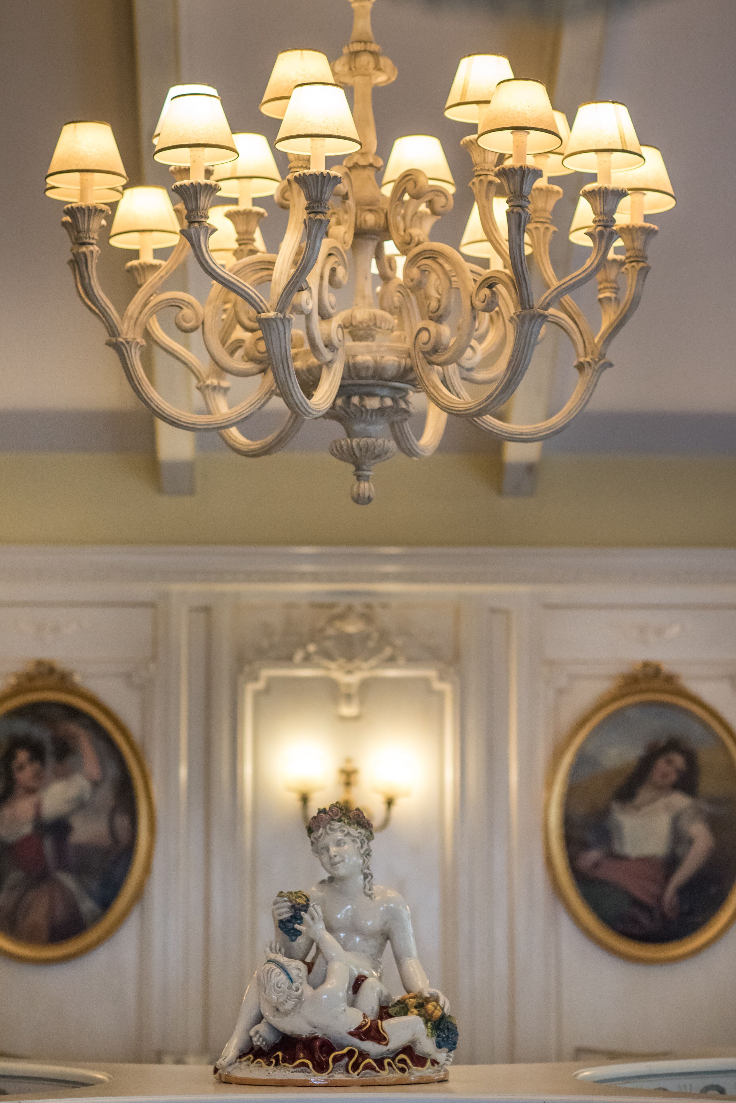 A chandelier with multiple lamps, a decorative statue, and two framed paintings on the wall.