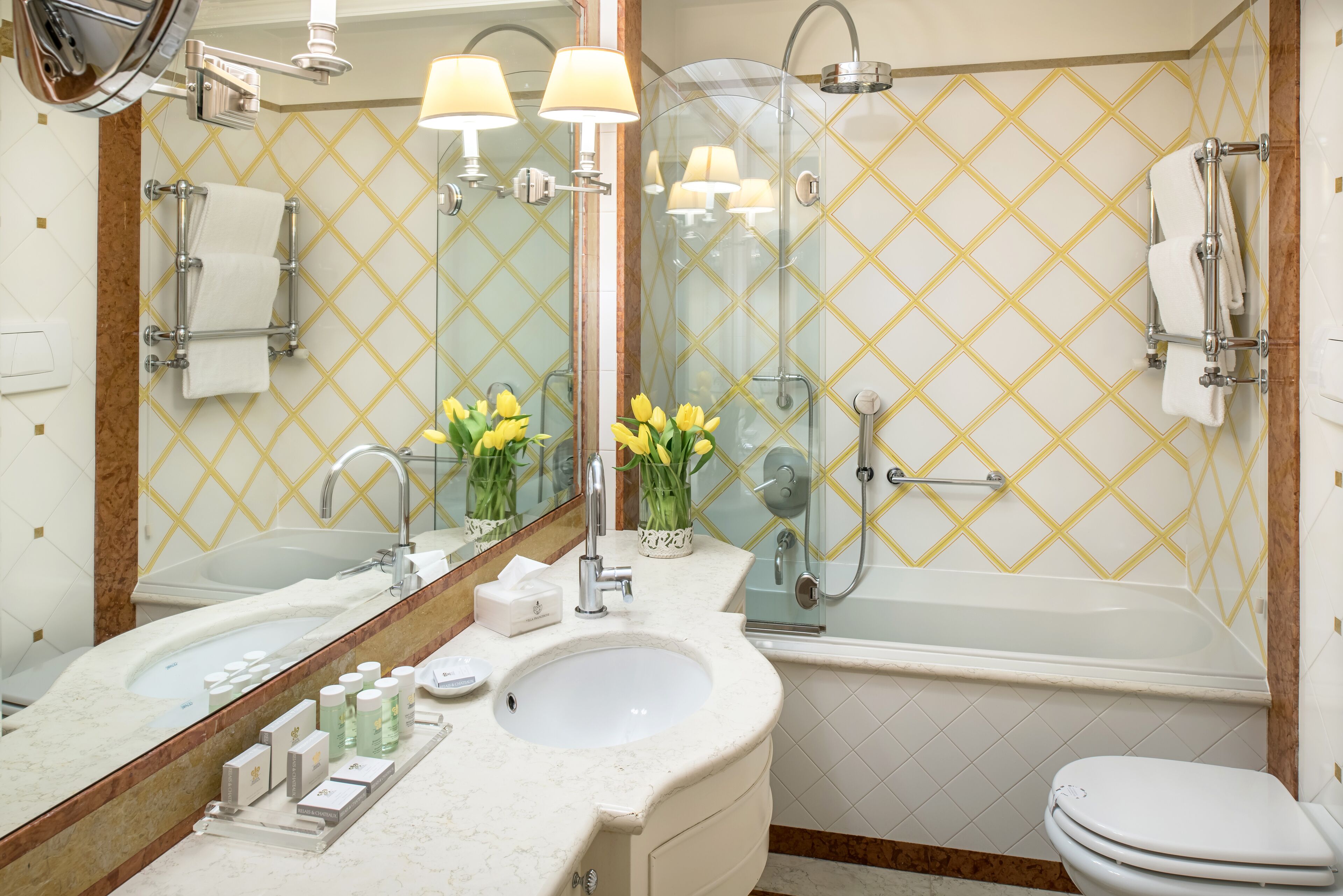 A modern bathroom with a large mirror, dual sinks, a bathtub, and a toilet.
