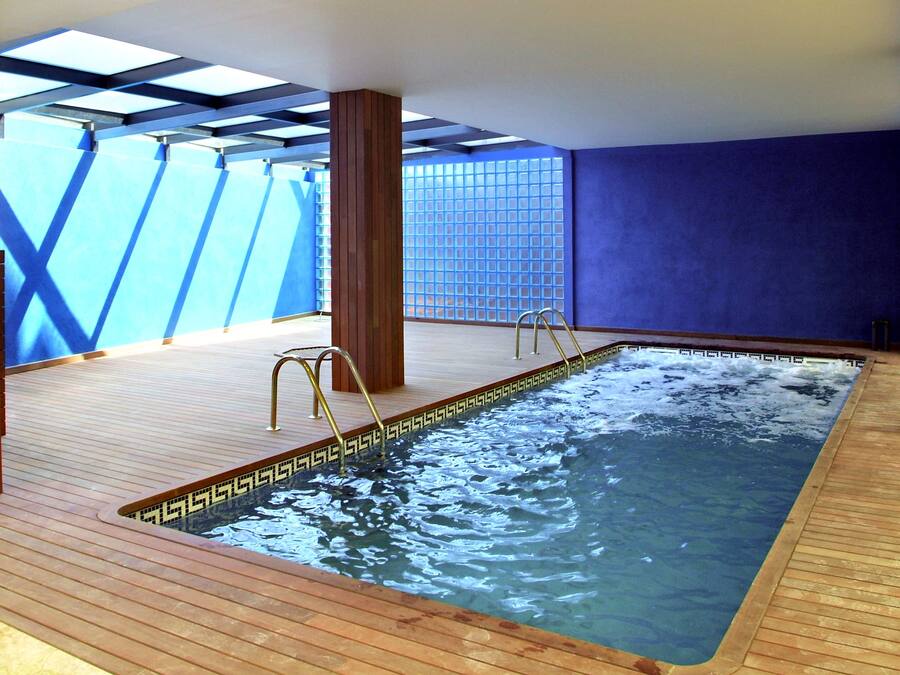 A hot tub in a room with a wooden floor, a blue wall, and a view of the sky.